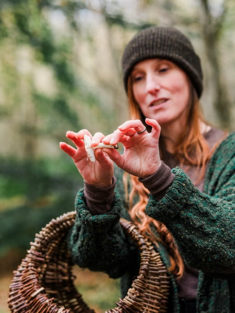 Bex Northman holding up a small mushroom and a foraging basket, explaining how to check it