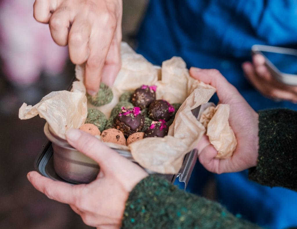 Hands sharing a tin of homemade wild food bites wrapped in baking paper